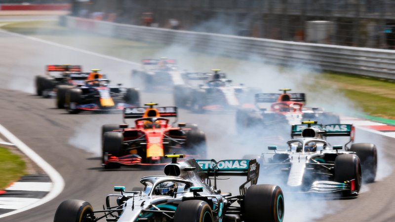 F1英国大奖赛正赛发车瞬间，多辆赛车在银石赛道并排驶过第一个弯道